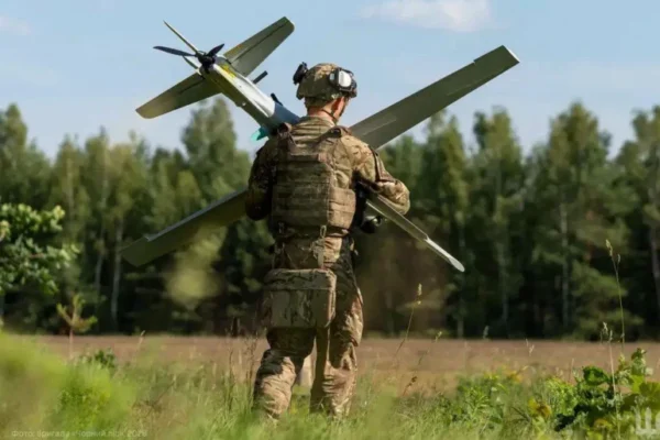 Soldat transportând dronă mare pe câmp